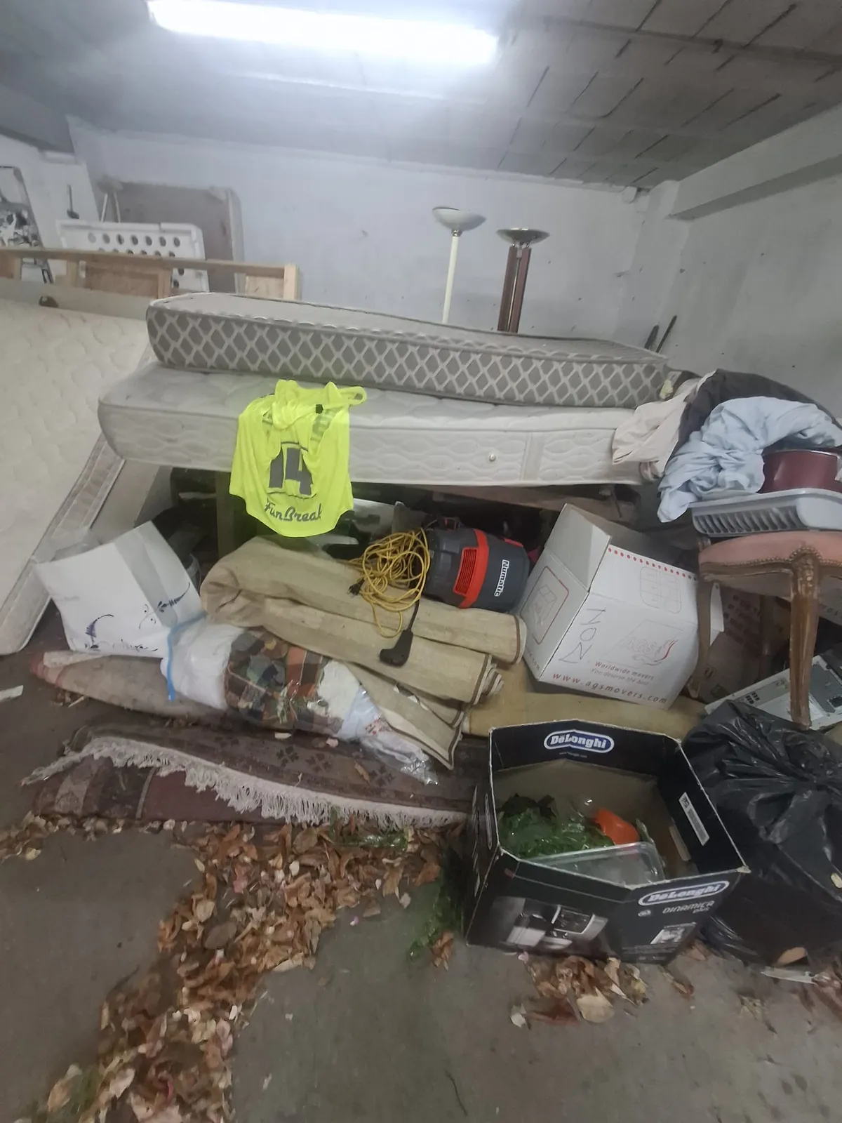 Cave encombrée de matelas, sommiers, tapis roulés et cartons avant débarras